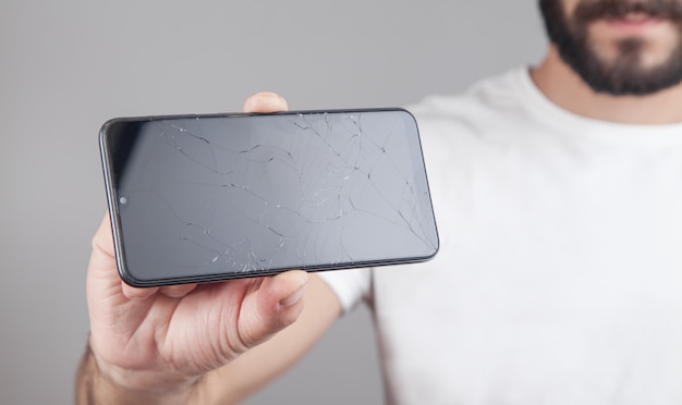 Homem segurando smartphone quebrado preto. tela quebrada