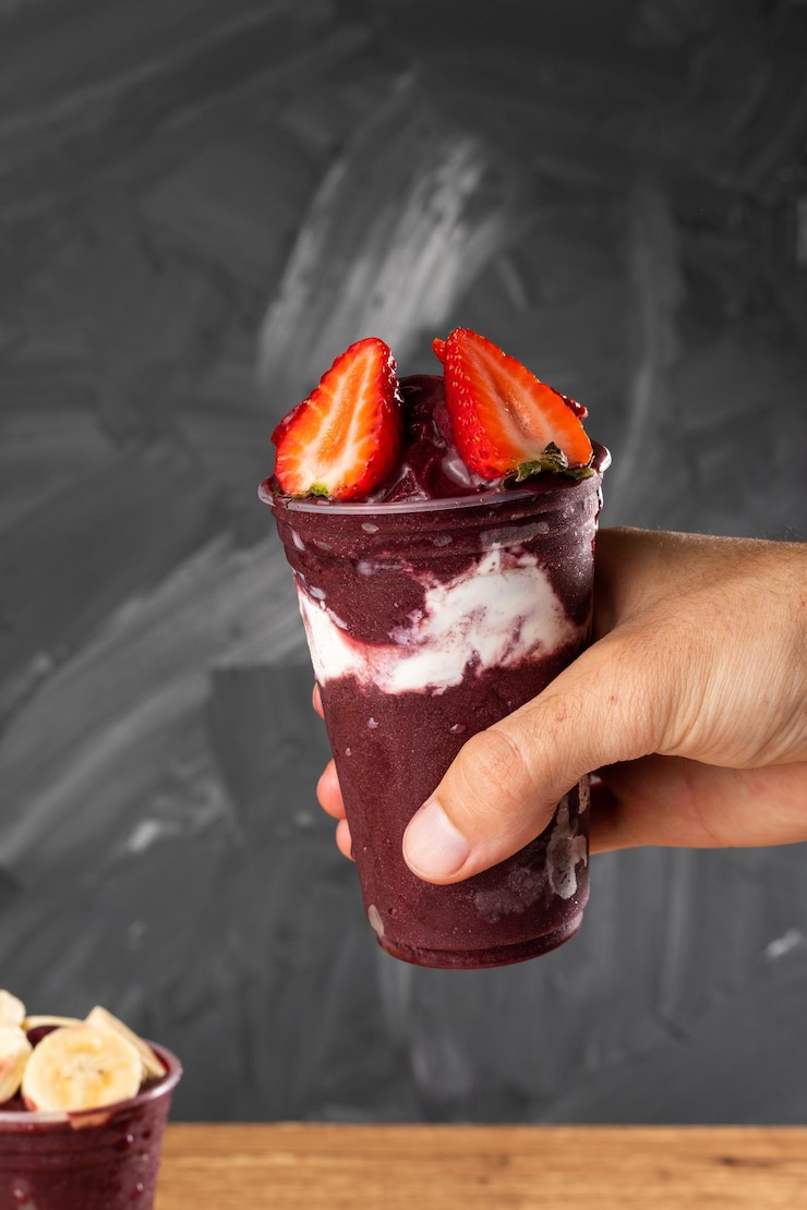 Foto homem segurando sorvete de frutas vermelhas congeladas em copo plástico com fundo cinza de morango