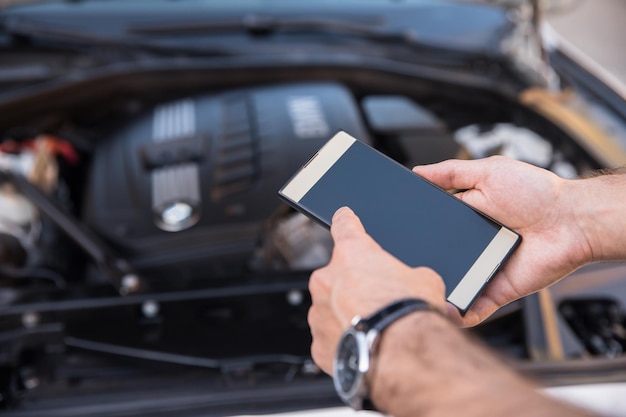 Homem segurando telefone com carro quebrado