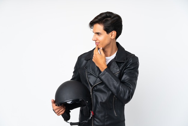 Homem segurando um capacete de moto sobre parede branca isolada, pensando uma idéia