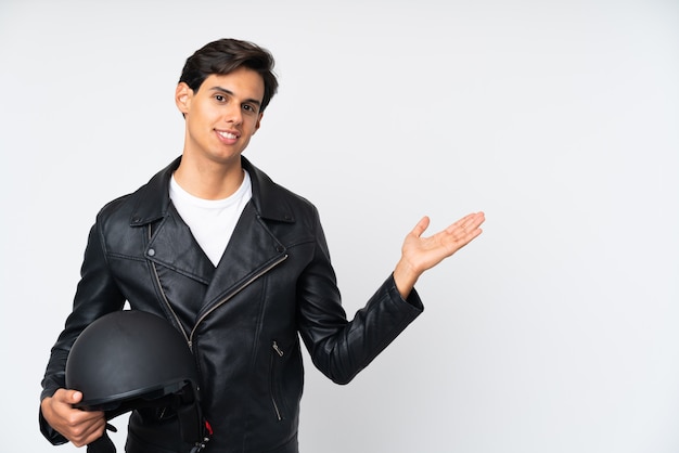 Homem segurando um capacete de moto sobre parede branca segurando copyspace imaginário na palma da mão