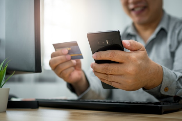 Homem segurando um cartão de crédito e usando smartphone para pagamento online