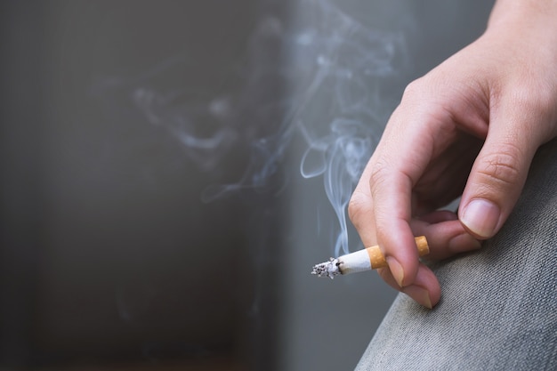 Homem segurando um cigarro na mão. a fumaça do cigarro se espalhou. sombrio