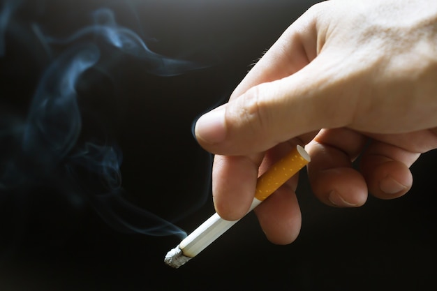 Homem segurando um cigarro na mão. a fumaça do cigarro se espalhou.