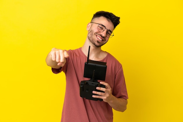 Homem segurando um controle remoto de drone isolado em um fundo amarelo apontando para a frente com uma expressão feliz