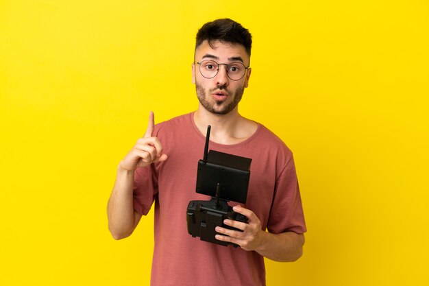 Homem segurando um controle remoto de drone isolado em um fundo amarelo com a intenção de perceber a solução enquanto levanta um dedo