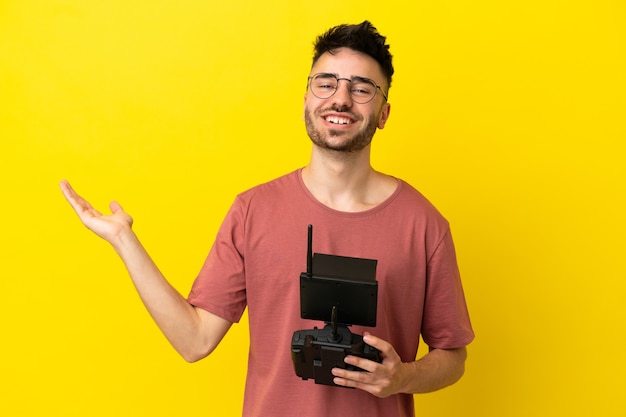 Homem segurando um controle remoto de drone isolado em um fundo amarelo, estendendo as mãos para o lado para convidar para vir