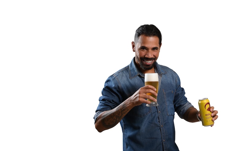 Foto homem segurando um copo com cerveja e olhando para a câmera faz um gesto oferecendo a bebida