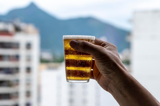 Homem segurando um copo de cerveja no fundo desfocado da cidade urbana