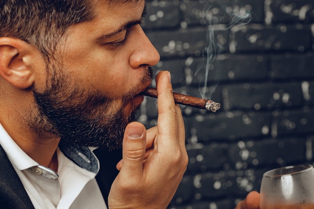 Foto homem segurando um copo de uísque e um cigarro aceso nas mãos fecha