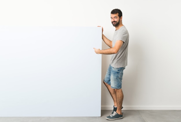 Foto homem segurando um grande cartaz vazio azul e apontando-o