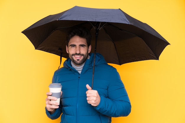 Homem segurando um guarda-chuva sobre parede amarela isolada