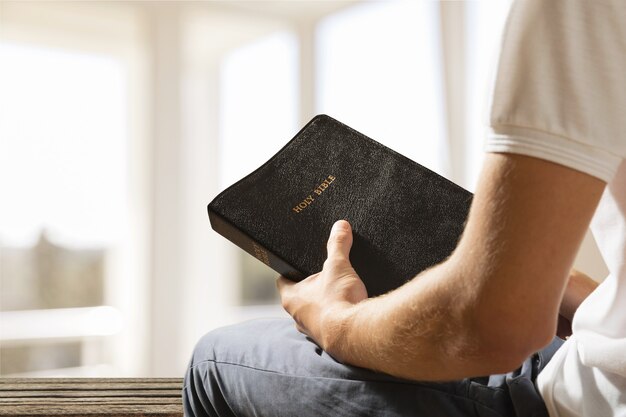 Homem segurando um livro da Bíblia sobre fundo verde