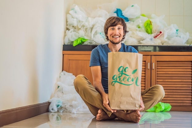 Homem segurando um pacote com a inscrição go green em meio a uma pilha de sacos plásticos conceito de lixo zero o conceito do dia mundial do meio ambiente