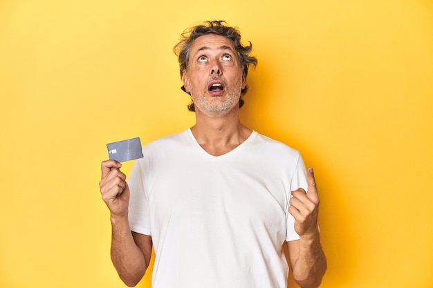 Homem segurando um pano de fundo de estúdio amarelo de cartão de crédito apontando de cabeça para baixo com a boca aberta