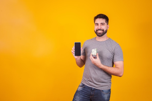 Homem segurando um pedaço de queijo em uma mão e celular na outra com tela em branco para espaço de texto. Conceito de anúncio da empresa de queijo. Entrega de queijo e compras online