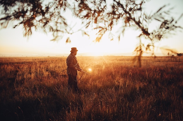 Homem segurando um rifle no campo contra o céu durante o pôr do sol