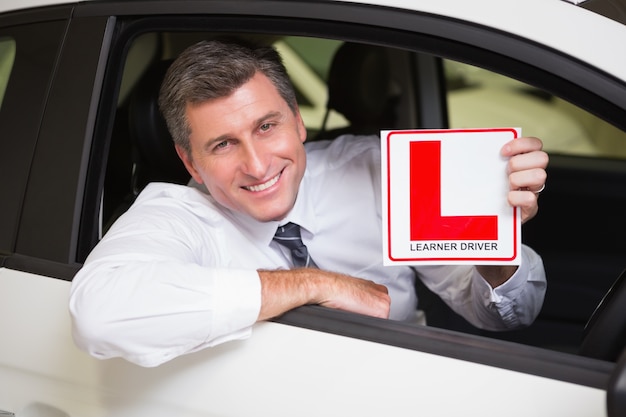 Homem segurando um sinal de motorista do aprendiz sentado ao volante