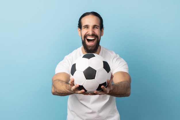 Homem segurando uma bola de futebol na mão e olhando para a câmera com expressão facial animada