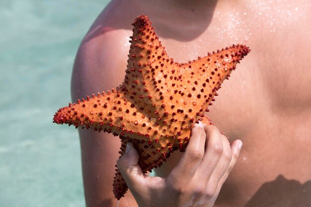 Homem segurando uma estrela do mar vermelha na mão com o oceano ao fundo Venezuela