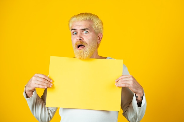 Homem segurando uma folha de papel em branco isolada em fundo amarelo