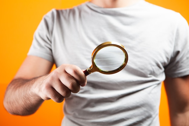 Foto homem segurando uma lupa em fundo laranja