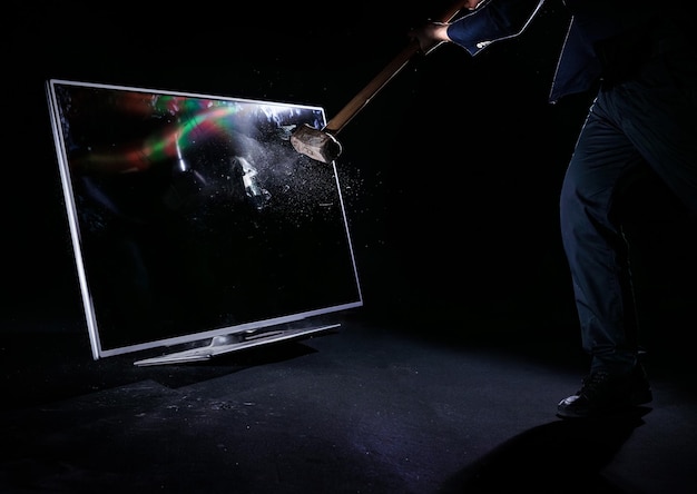 Homem segurando uma marreta batendo e quebrando uma televisão de plasma isolada em um fundo preto