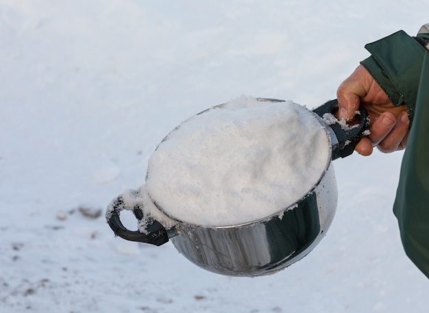 Homem segurando uma panela cheia de neve, por derreter na água potável.