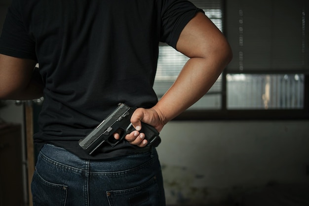 Foto homem segurando uma pistola de pé em uma sala em preto conceito de criminoso de assassinato de assassinato