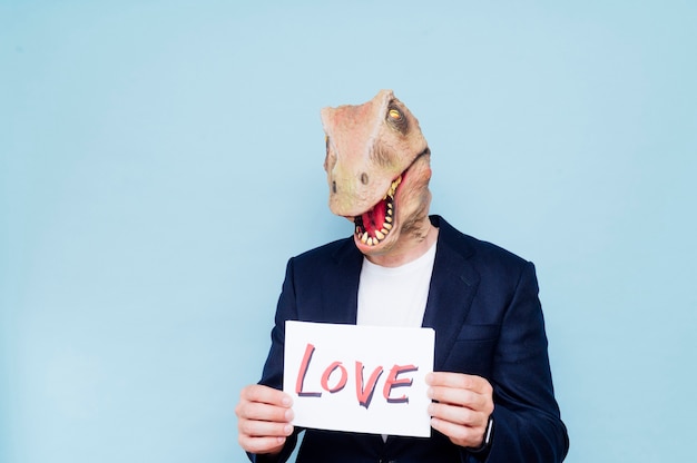 Homem segurando uma placa que diz amor. Máscara de dinossauro com fundo azul