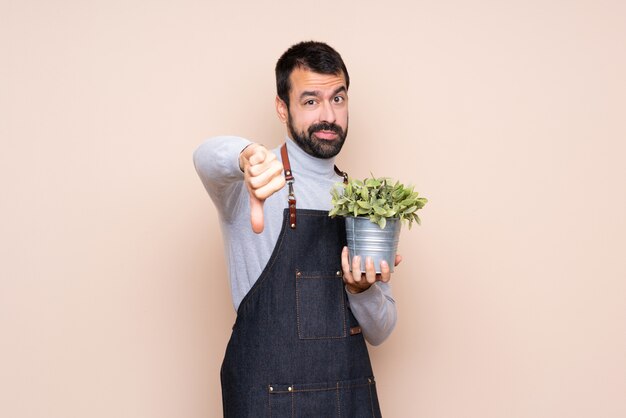 Homem segurando uma planta mostrando o polegar para baixo com expressão negativa