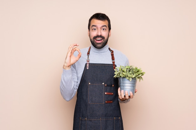 Homem segurando uma planta surpreso e mostrando sinal ok