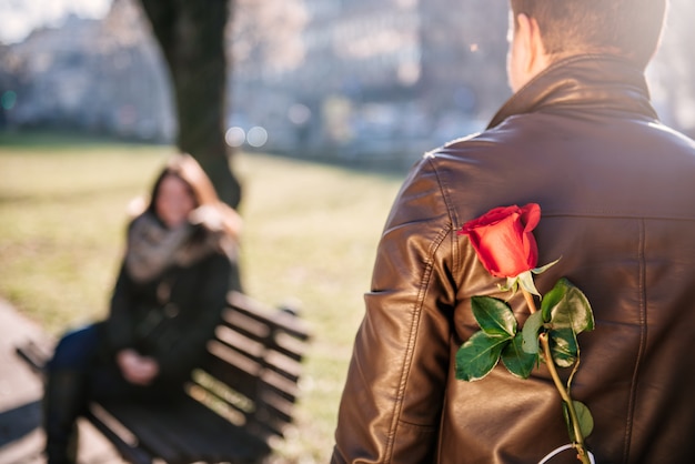 Homem segurando uma rosa vermelha nas costas