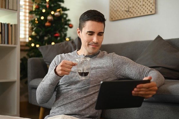 Homem segurando uma xícara de café e usando tablet digital em casa