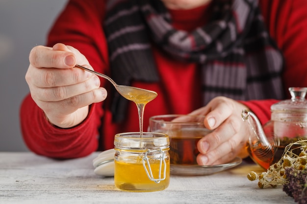 Homem segurar a xícara de chá quente em copo de vidro, pote de mel, concha de sopa de mel na mesa de madeira velha