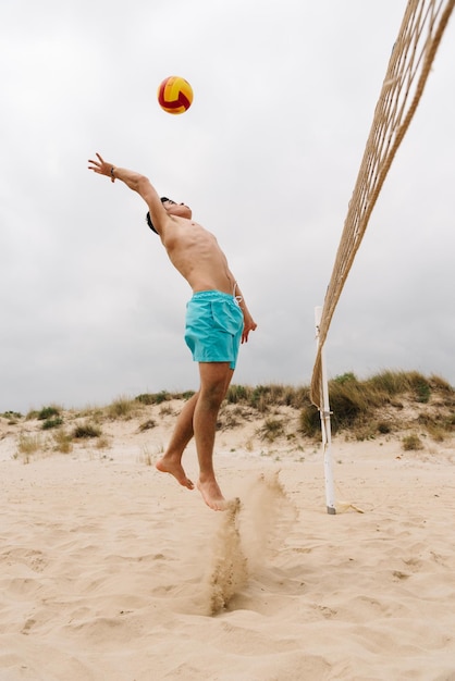 Homem sem camisa a jogar voleibol na praia.