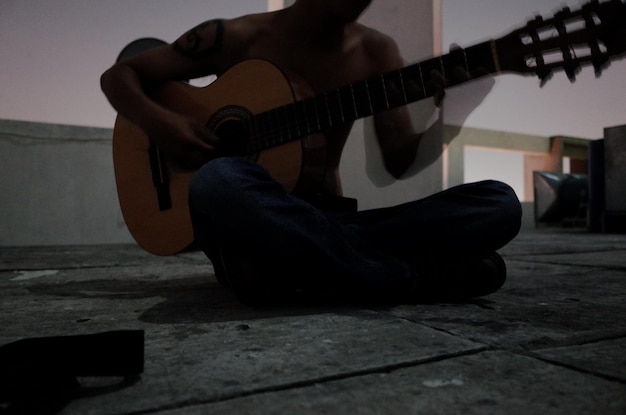 Foto homem sem camisa a tocar guitarra no terraço