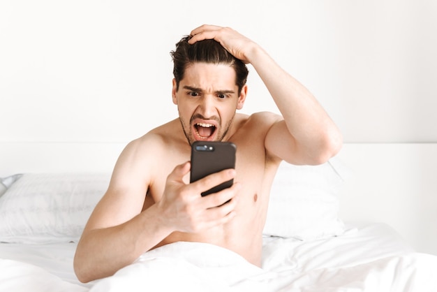 Homem sem camisa chocado olhando para o celular