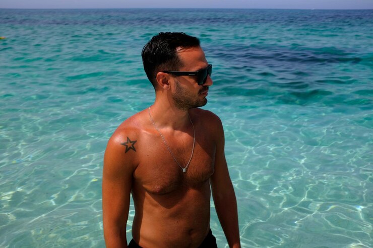 Foto homem sem camisa com óculos de sol de pé no mar em um dia ensolarado