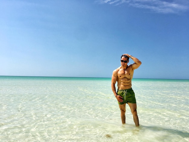 Foto homem sem camisa de pé no mar em um dia ensolarado