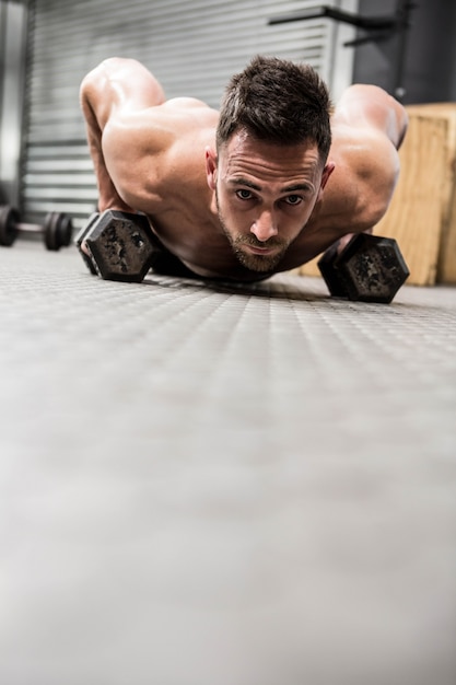 Foto homem sem camisa fazendo push-up com halteres no ginásio crossfit