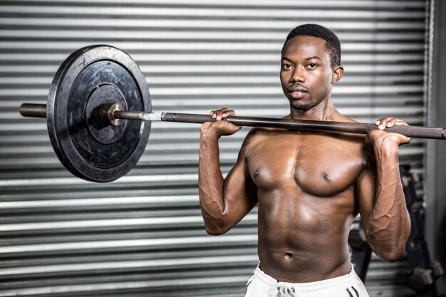 Homem sem camisa, levantando a barra no ginásio crossfit