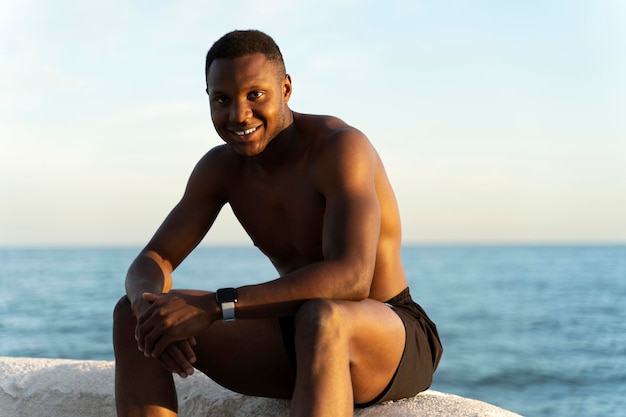 Homem sem camisa na praia aproveitando o sol enquanto sorri para a câmera