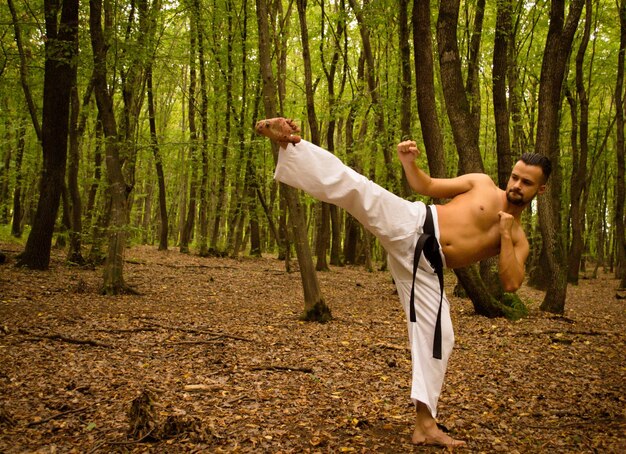 Homem sem camisa praticando karatê contra árvores na floresta