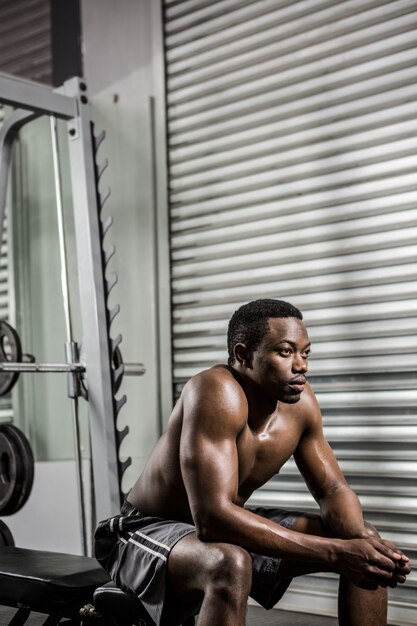 Homem sem camisa, sentado no banco no ginásio crossfit