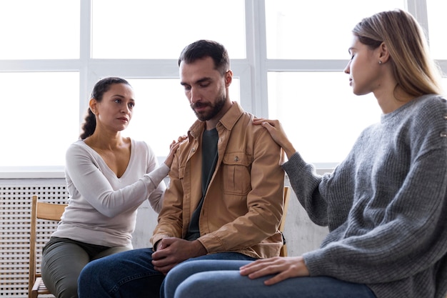 Foto homem sendo consolado por mulheres em sessão de terapia em grupo