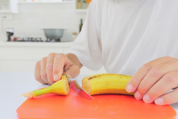 Homem sênior a cortar banana na cozinha