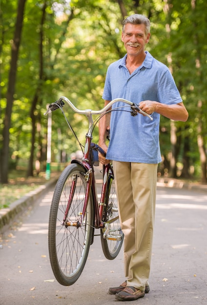 Homem sênior alegre com a bicicleta no parque.