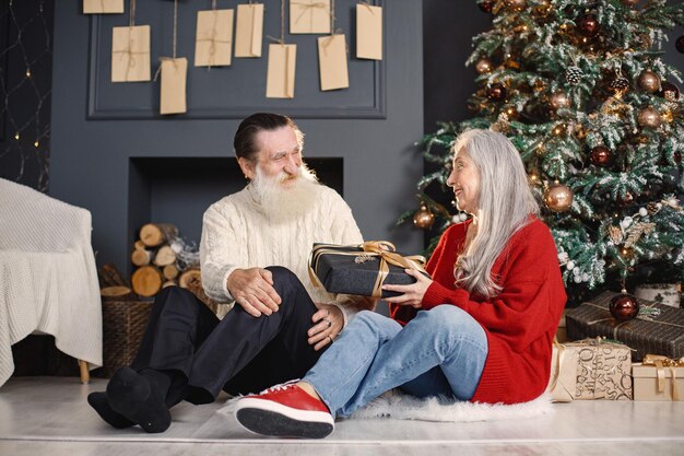 Homem sênior apresentando presente de natal para sua esposa sentada perto da árvore de natal