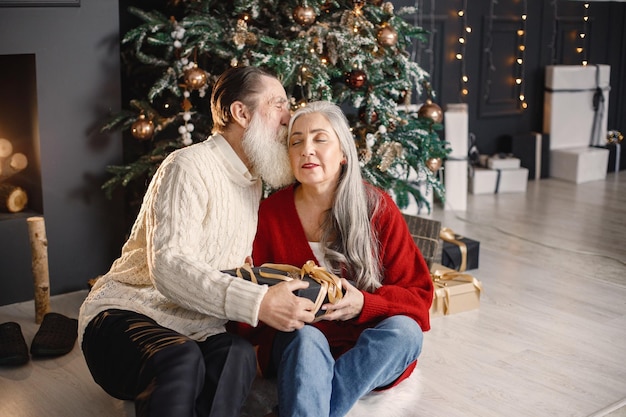 Homem sênior apresentando presente de natal para sua esposa sentada perto da árvore de natal